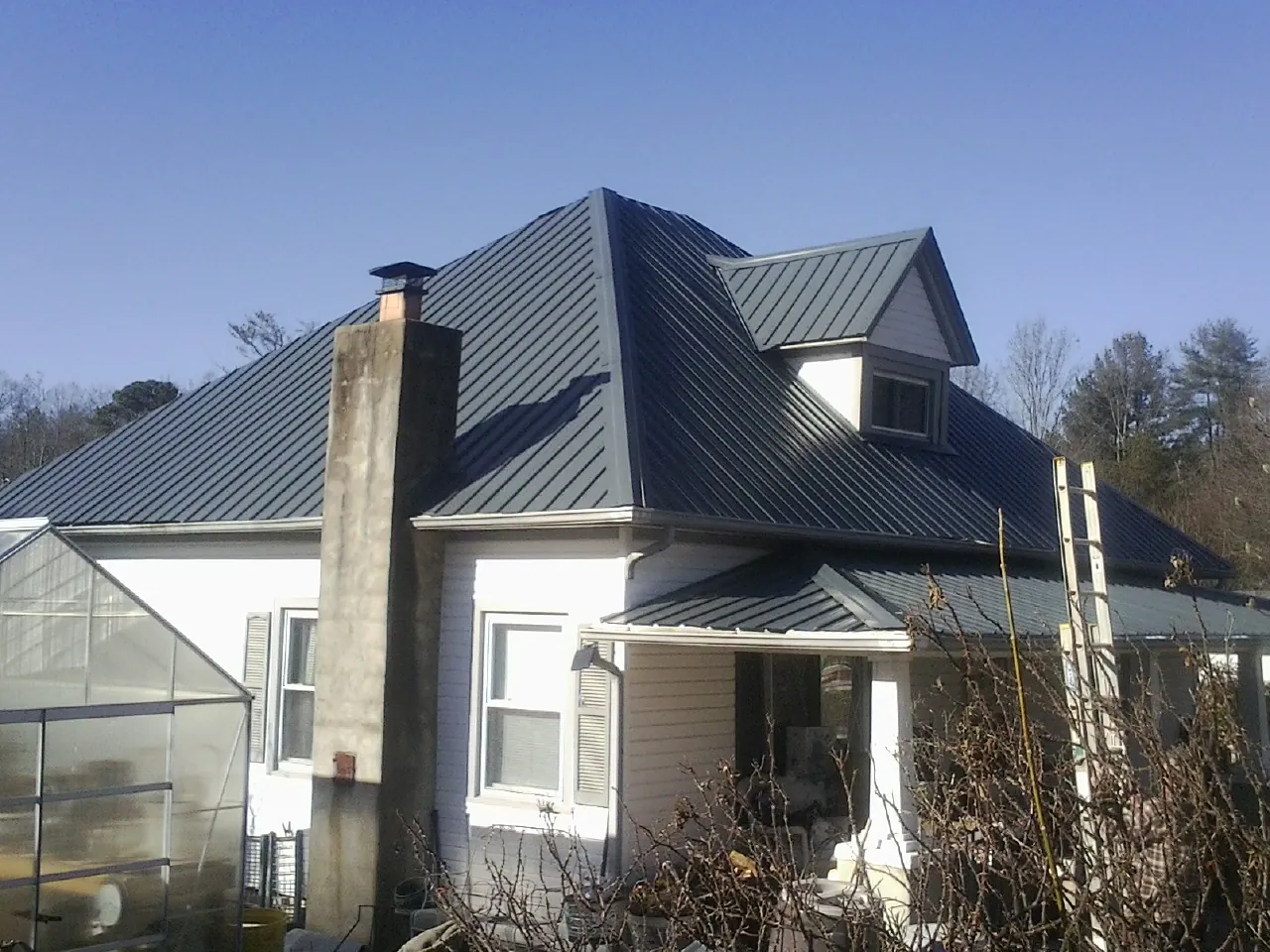 Dark blue standing seam metal roof on a white farmhouse with dormer — Slate & Tile Roof Repair by Roofing Brothers in Thornwood