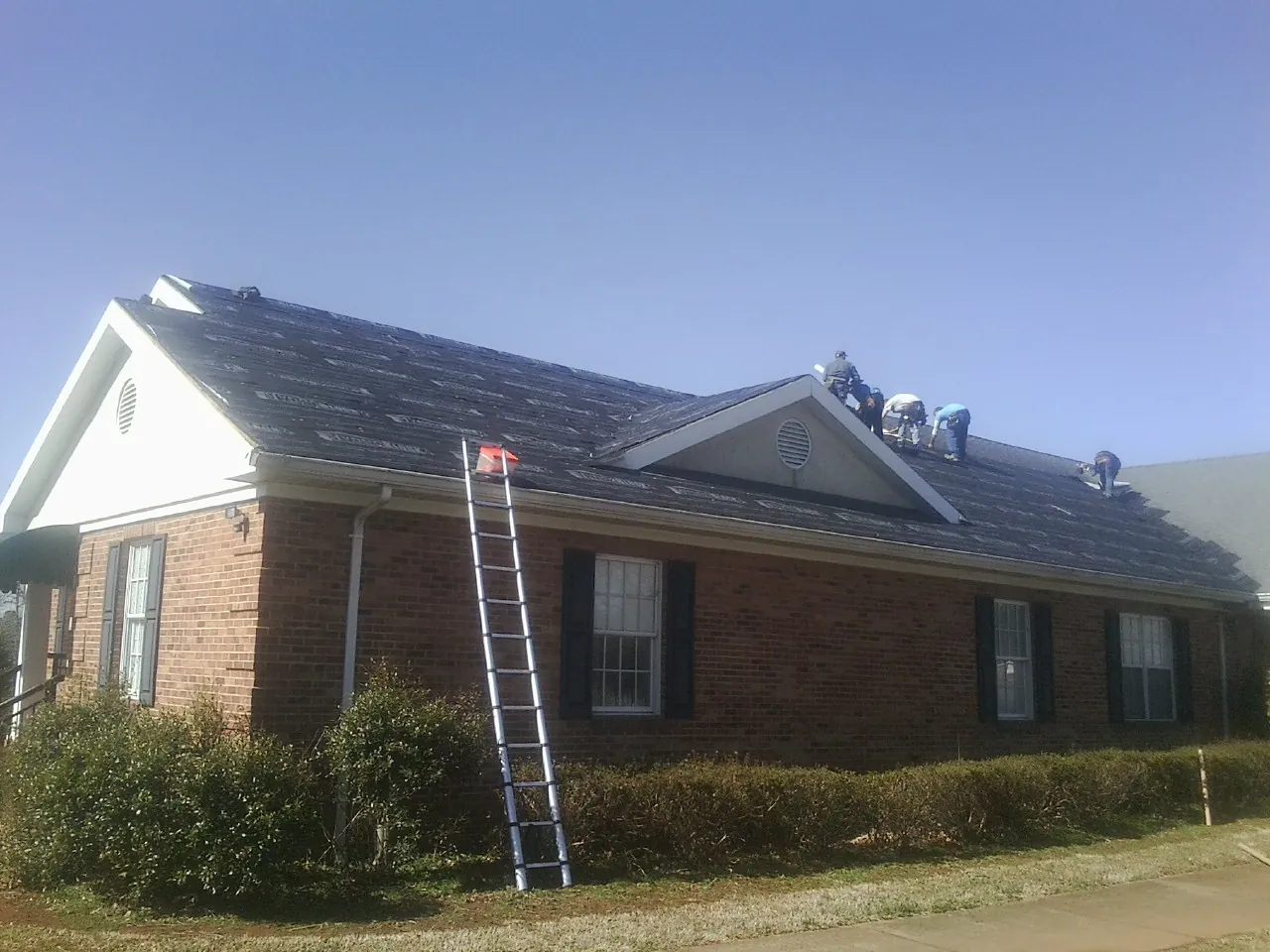 Crew tearing shingles off a brick ranch roof with a ladder set — Emergency Roof Repair work by our crew in Thornwood