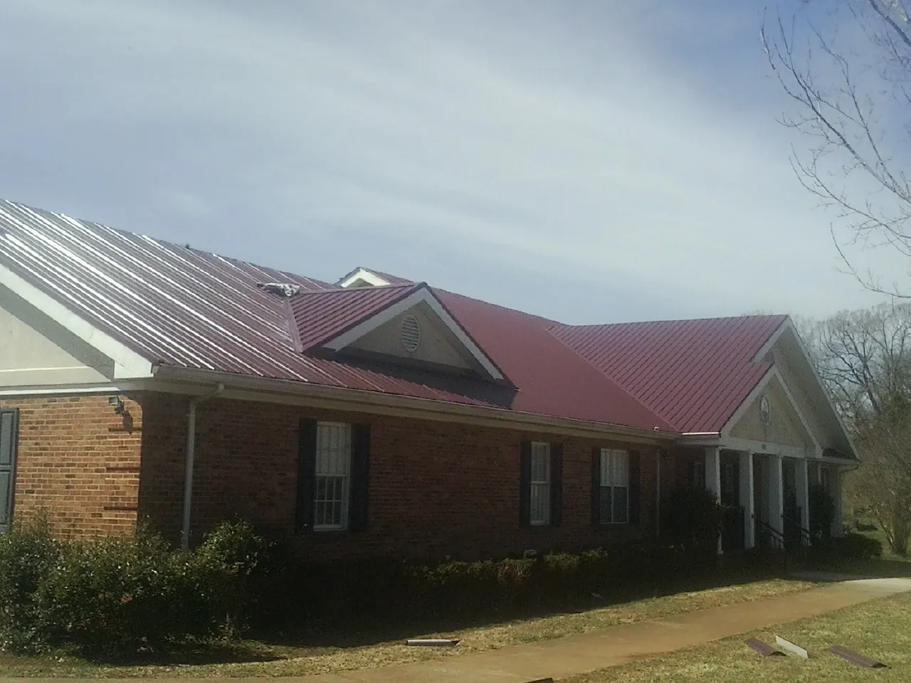 Red metal roof with gabled entries on a long brick building, from a Hail Damage Roof Repair job in Thornwood