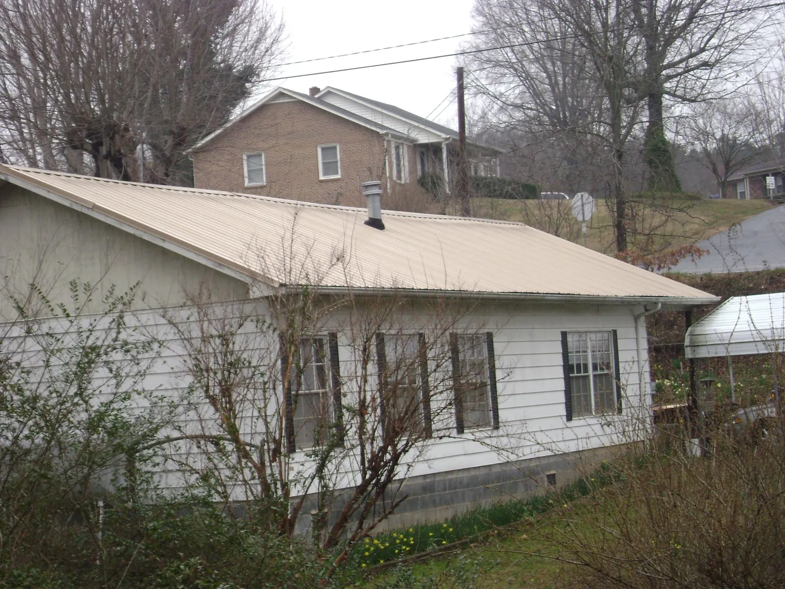 Tan metal roof on a white sided house set into a hillside — Commercial Roofing by Roofing Brothers in Thornwood