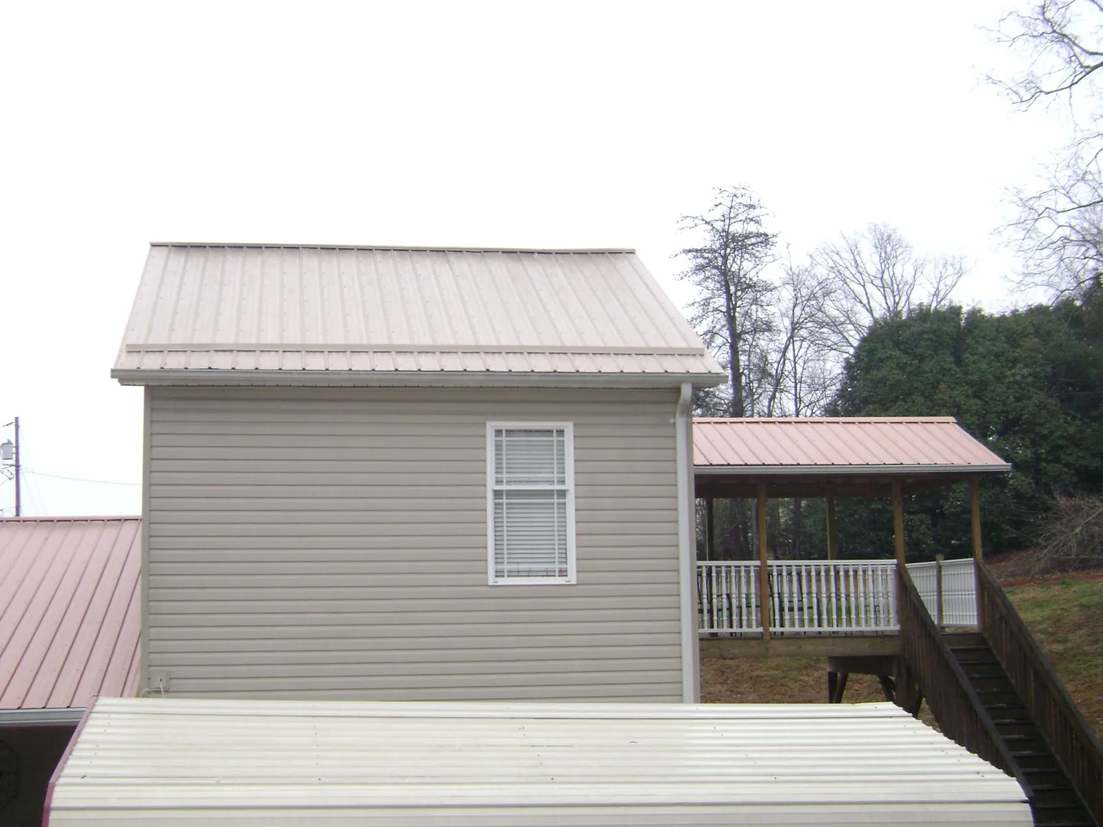 Tan metal roofs on a two story addition and attached porch, from a Roof Replacement job in Thornwood
